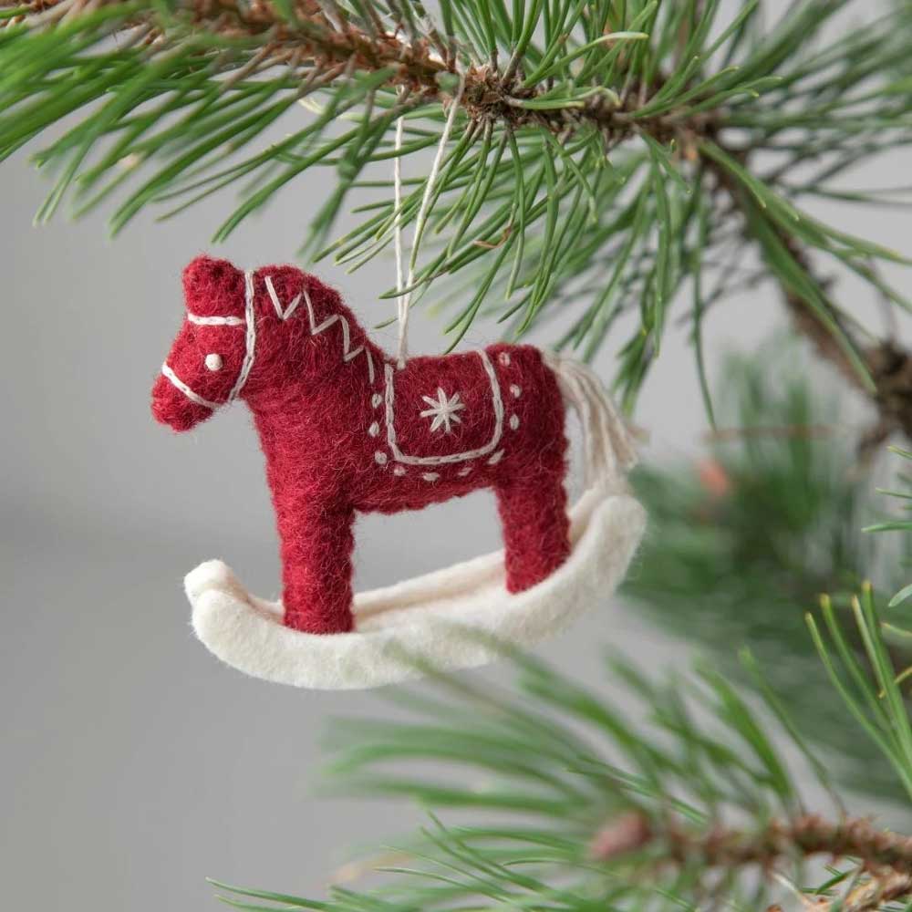 Das Schaukelpferd-Ornament aus Filz von Gry & Sif mit weißer Stickerei baumelt an einem grünen Ast.