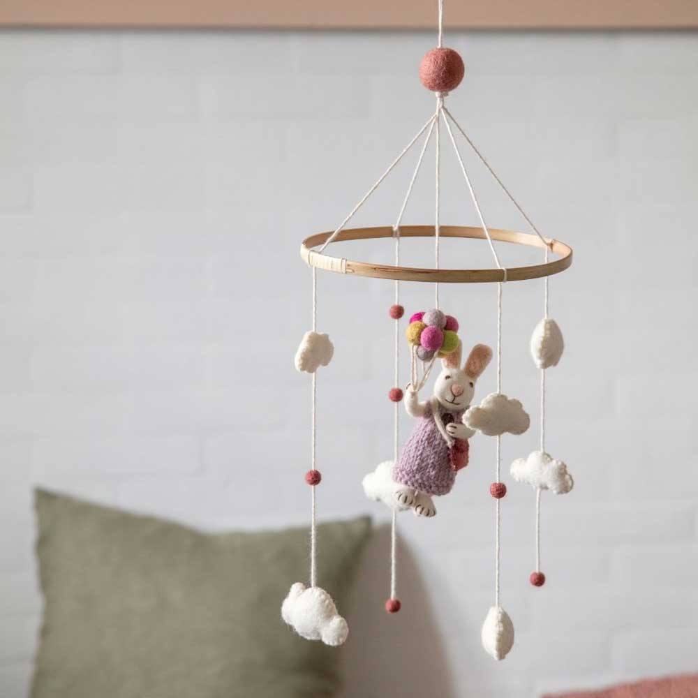 Ein Baby-Mobile „Hase Mädchen mit Luftballons“ von Gry & Sif hängt mit Wolken und kleinen Bällen verziert von der Decke und steht vor einer weißen Backsteinwand.