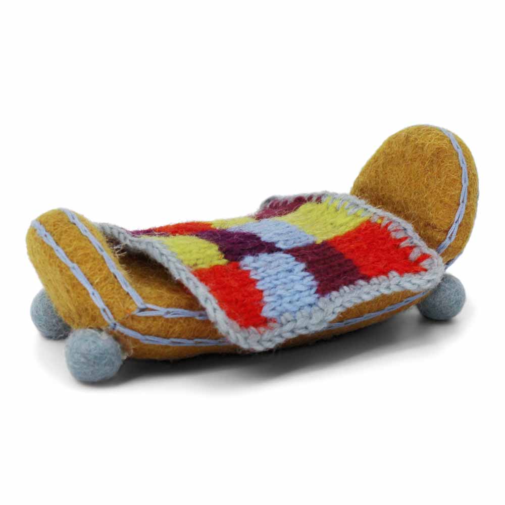 Eine kleine, bunte Strickdecke bedeckt ein Miniaturbett aus gelbem Filz von Gry & Sif – Bett mit Decke Filz mit blauen Kugelfüßen.