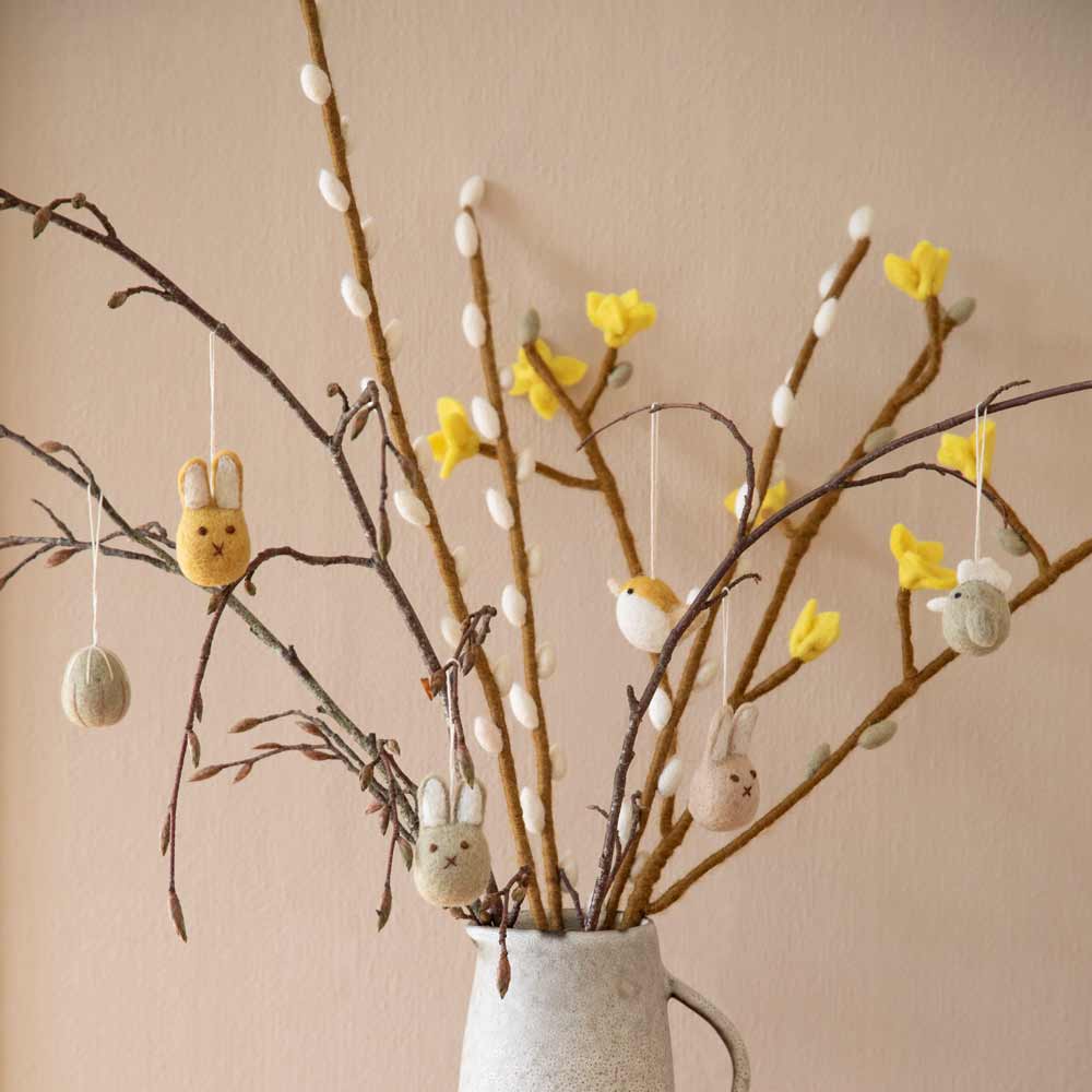 Ein Gry & Sif - Weidenkätzchen Filz aus dekorativen Zweigen mit Osterornamenten und gelben Blumen.