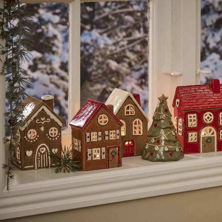 Eine Fensterbank ist mit einer Lebkuchen-Rundbogentür von Ib Laursen - Haus für Teelicht Stillenat und einer Weihnachtsbaumfigur vor einer verschneiten Außenkulisse geschmückt.