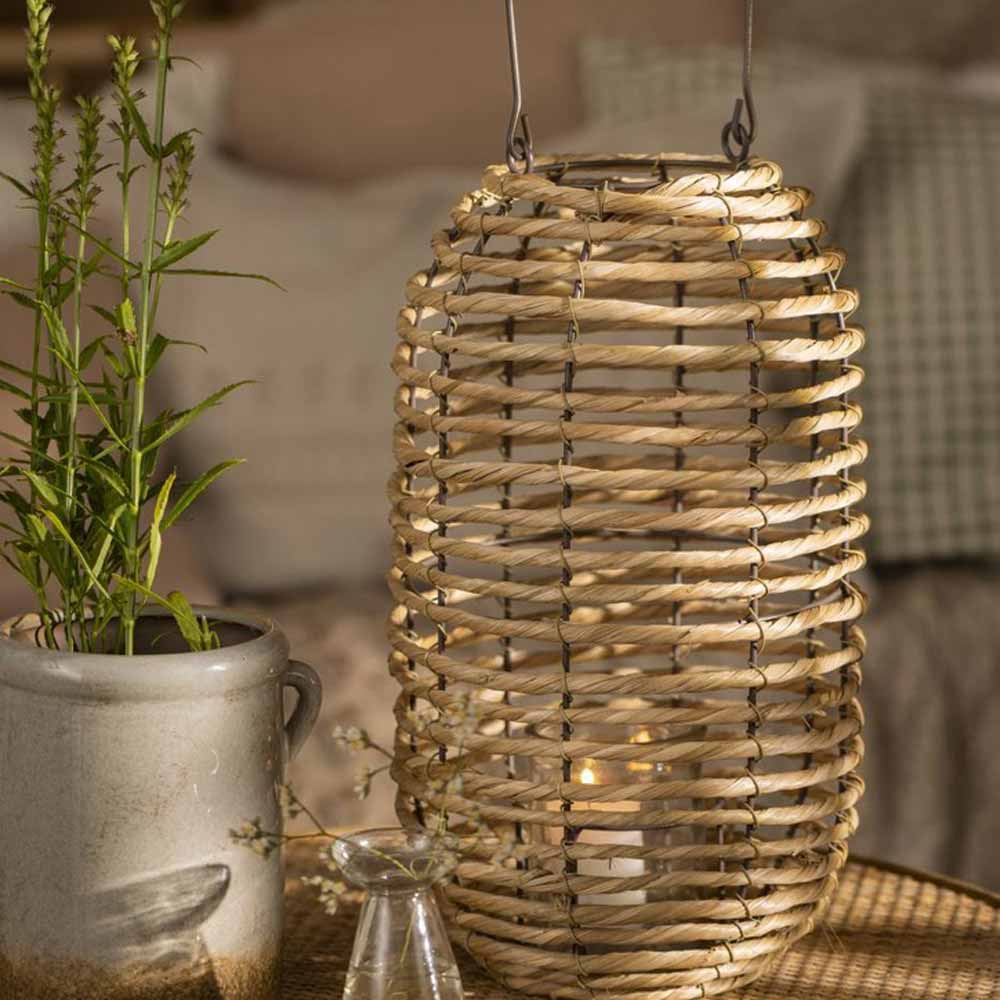 Gewebte Laterne von Ib Laursen auf einer rustikalen Tischplatte mit einer Topfpflanze und einer Glasvase.