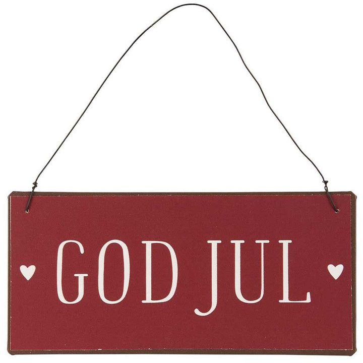 Das Ib Laursen - Metallschild God Jul ist ein rechteckiges rotes Schild mit der weißen Aufschrift „GOD JUL“ und ist auf jeder Seite mit kleinen Herzsymbolen verziert und hängt an einem schwarzen Draht.