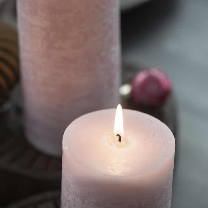 Beleuchtete Ib Laursen - Rustikale Kerze Höhe: 7,5 cm mit einer hohen, unbeleuchteten rosa Kerze und Dekoartikeln im Hintergrund auf grauem Untergrund.