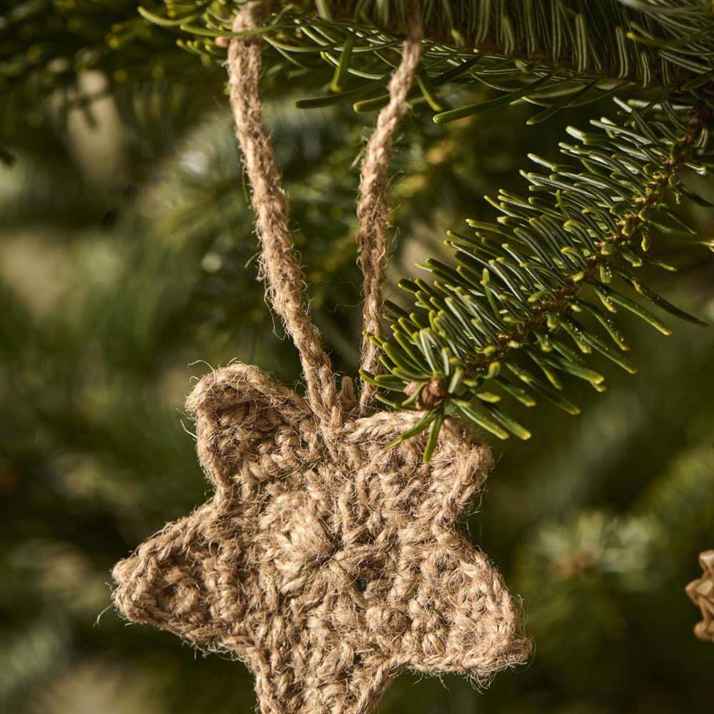 Ein sternförmiges, aus Jute gehäkeltes Ornament von Ib Laursen, das an einem grünen Tannenzweig hängt.