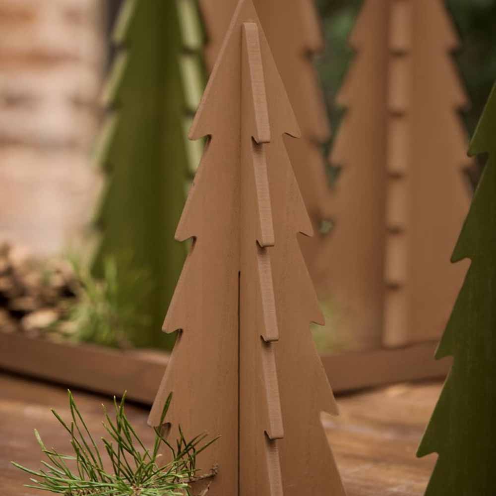 Nahaufnahme des Weihnachtsbaumschmucks „Tannenbaum stehend Holz“ von Ib Laursen in Form von Tannenbäumen in natürlichen Braun- und Grüntönen, platziert auf einer Holzoberfläche mit etwas Grün drumherum.