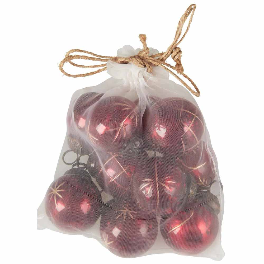 Ein Beutel mit Kordelzug, der kleine rote Weihnachtsornamente mit goldenen Gravuren von Ib Laursen enthält.