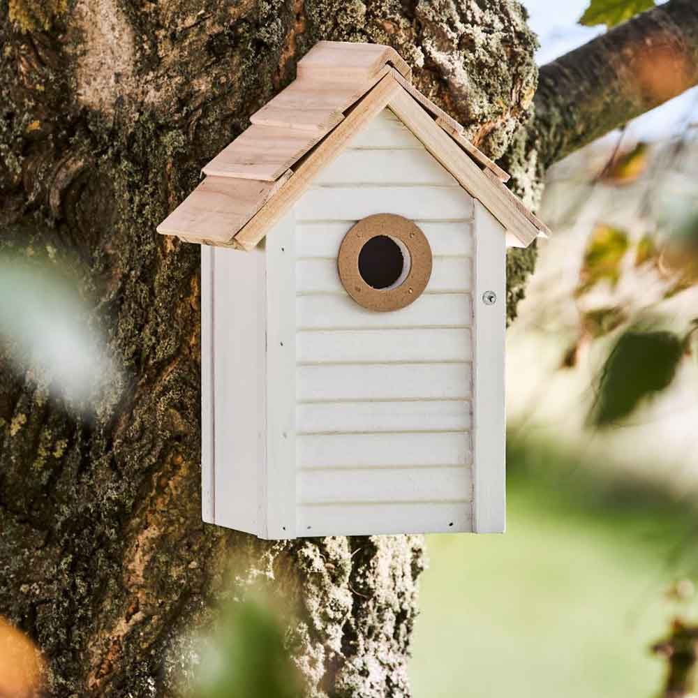 Das Ib Laursen - Vogelhaus weiß mit naturfarbigem Dach wird am Stamm eines Baumes montiert.