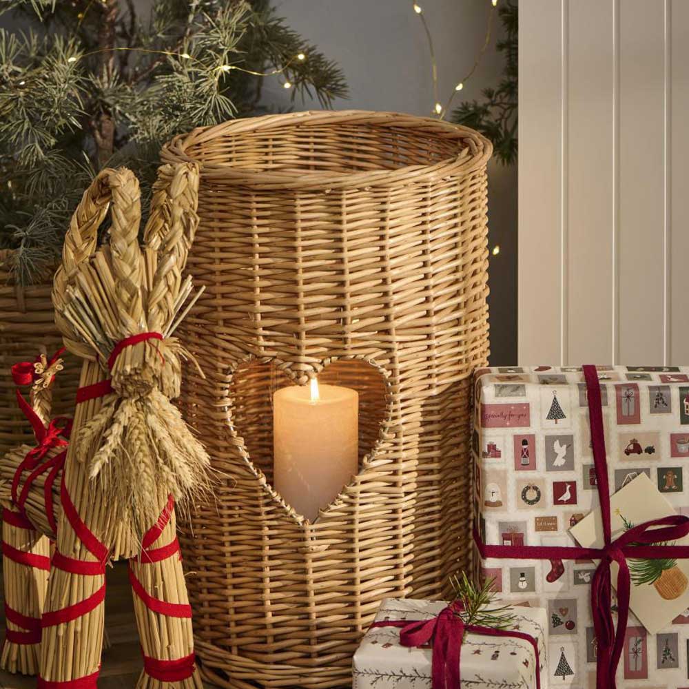 Ein Ib Laursen - Kerzenhalter im Landhausstil aus Rattan mit Herz und Glaseinsatz, umgeben von verpackten Geschenken und Strohornamenten, sorgt für einen festlichen Rahmen.