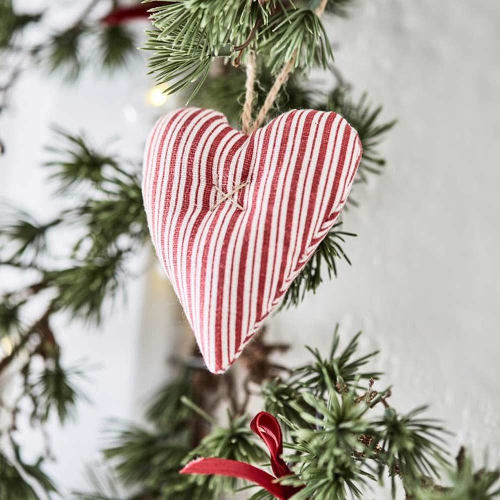 Eine Ib Laursen - Zederngirlande mit Zapfen-Kieferngirlande hängt an einer Schnur und ist neben anderen Weihnachtsdekorationen mit einem rot-weiß gestreiften Herzornament aus Stoff geschmückt.