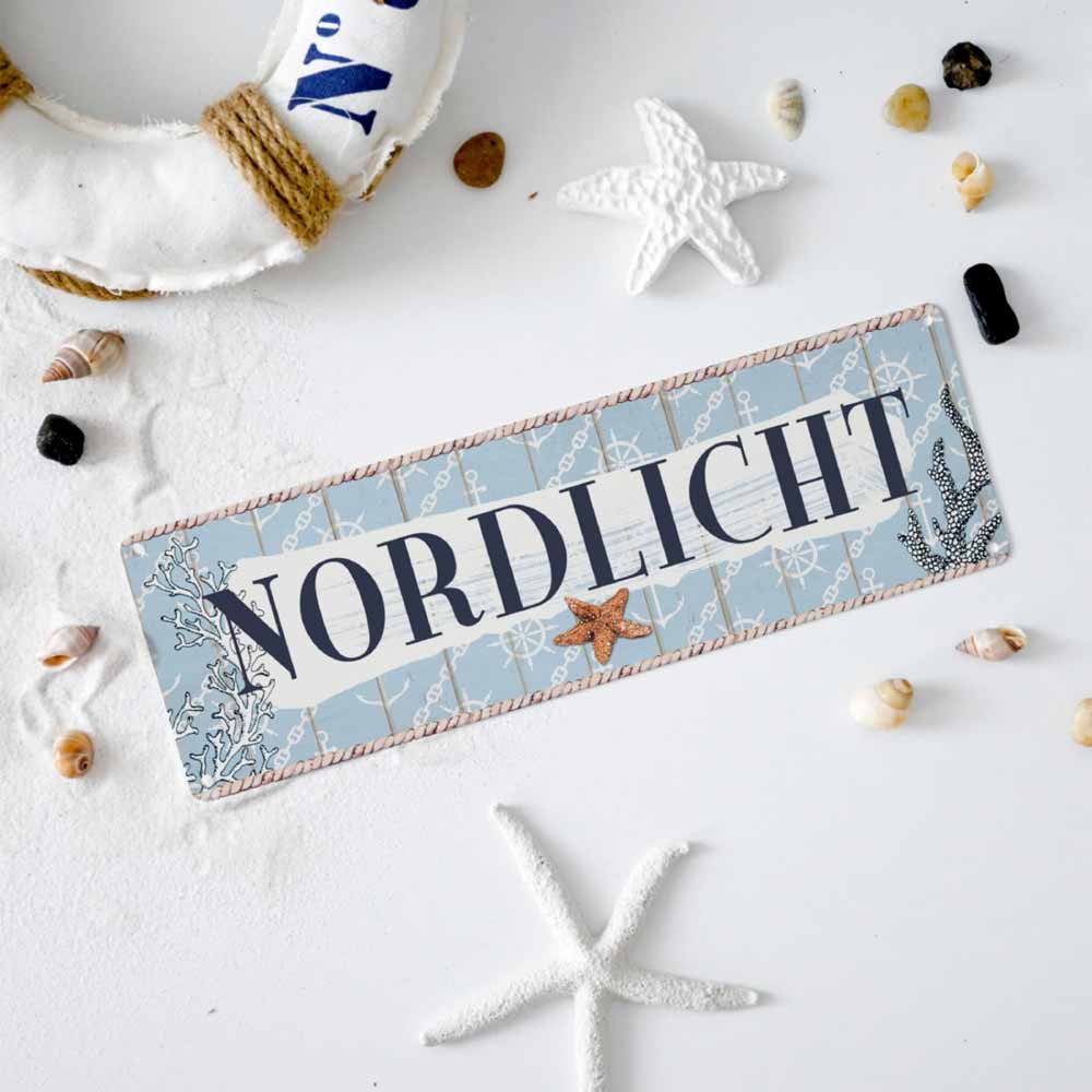 Ein rechteckiges Schild mit der Aufschrift „Interluxe Metallschild – Nordlicht“ in fetten Buchstaben, umgeben von nautischem Dekor, darunter Seesterne, Muscheln und ein kleiner Rettungsring.