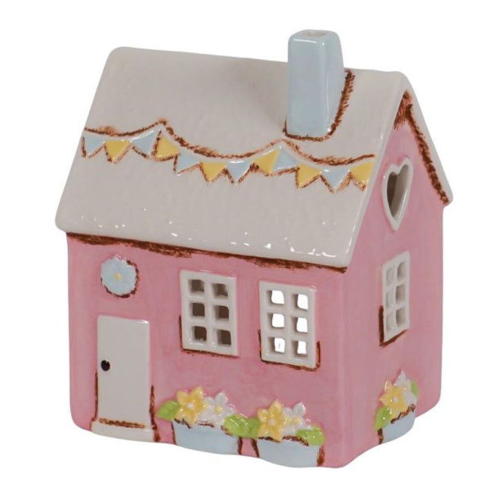 Das "Isabelle Rose - Keramik Haus als Teelichthalter im Landhausstil Rosa" ist ein kleines, rosafarbenes Keramikhaus mit grauem Dach, blauem Schornstein, Wimpeln, Blumenkästen und einem herzförmigen Fenster.