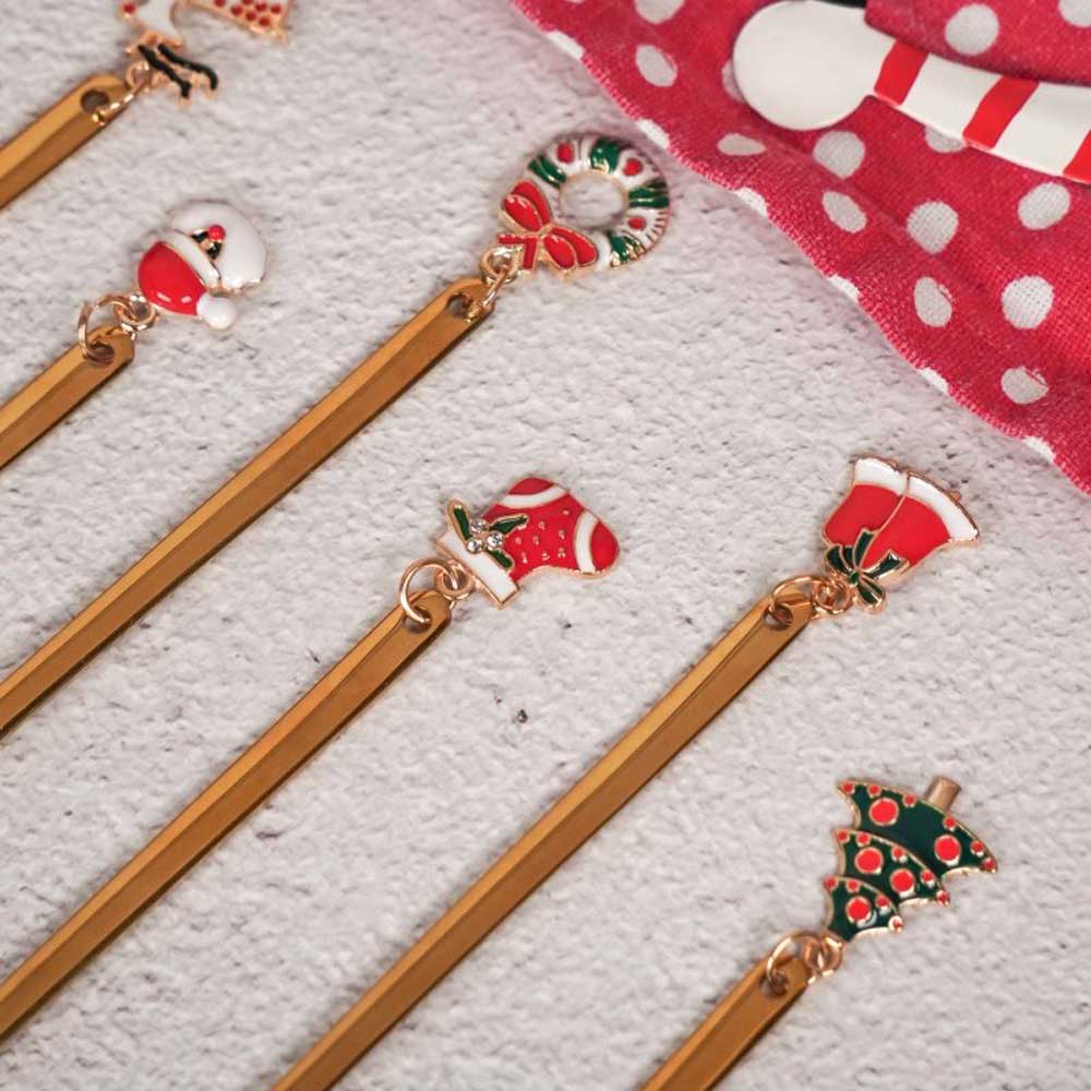 Ein Set goldfarbener Lesezeichen mit Weihnachtsmotiven, darunter Anhänger wie Weihnachtsmannmütze, Strumpf, Kranz, Zuckerstange und Weihnachtsbaum aus der Goldkollektion „Isabelle Rose – Weihnachtsgabel mit Anhänger 6er-Set“, ist elegant auf einem rot-weiß gepunkteten Tuch angeordnet.