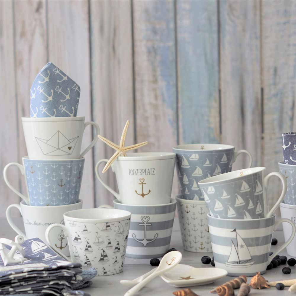 Eine Kollektion von Krasilnikoff - Happy Cup Anker graue Streifen in Blau und Weiß, mit Motiven von Ankern, Booten und Streifen. Servietten und ein Seestern sind um die Tassen herum angeordnet, alles vor einem Holzhintergrund.