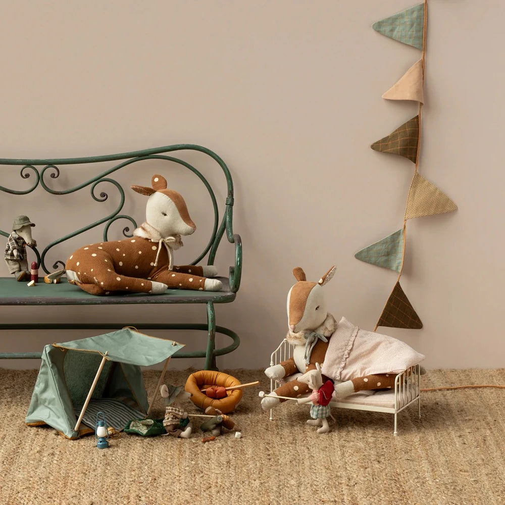 Maileg - Bambi-Plüschhirsche werden auf einer Bank und einem Spielzeugbett ausgestellt, umgeben von Mini-Campingrequisiten, kleinen Puppen und einem Wimpelbanner aus Stoff vor einer beigen Wand.