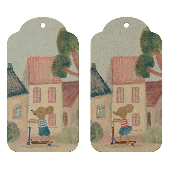 Der Maileg - Geschenkanhänger Maus 12 Stück zeigt eine Illustration einer Maus auf einem Roller vor Häusern, gedruckt auf zwei identischen, runden Anhängern mit Löchern zum Aufhängen.