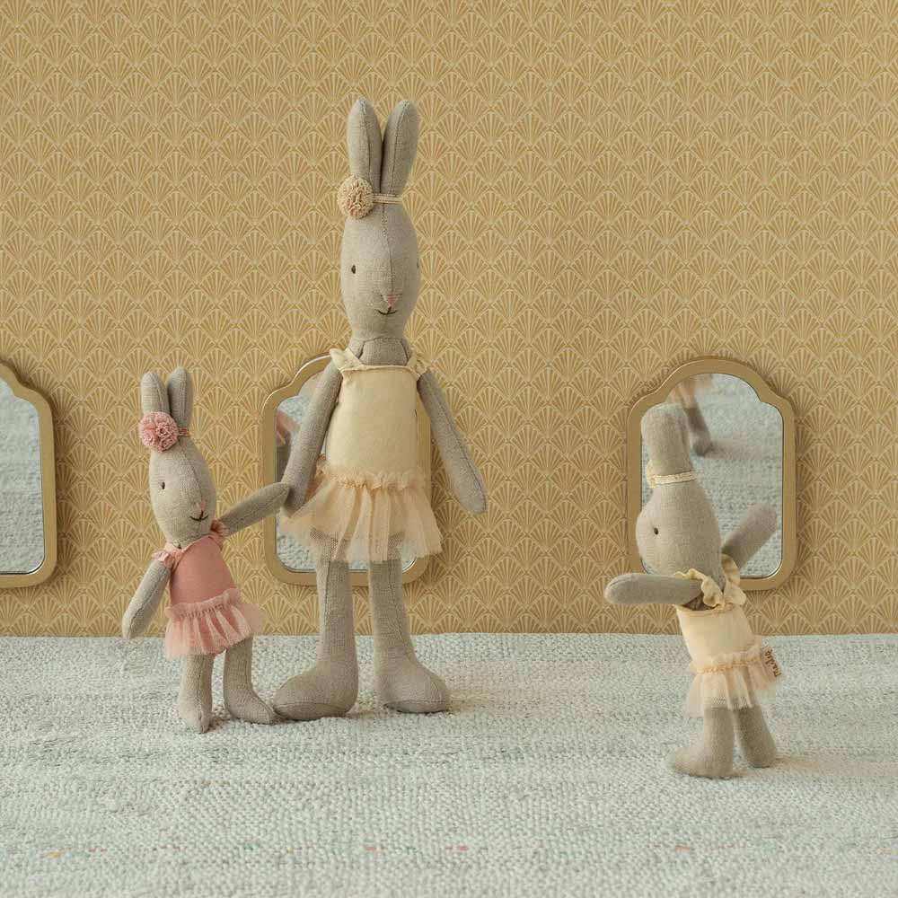 Drei Maileg - Hase Ballerina Micro Plüschkaninchen in pastellfarbenen Kleidern stehen auf einer strukturierten Oberfläche, mit gemusterter Tapete und kleinen Spiegeln im Hintergrund.