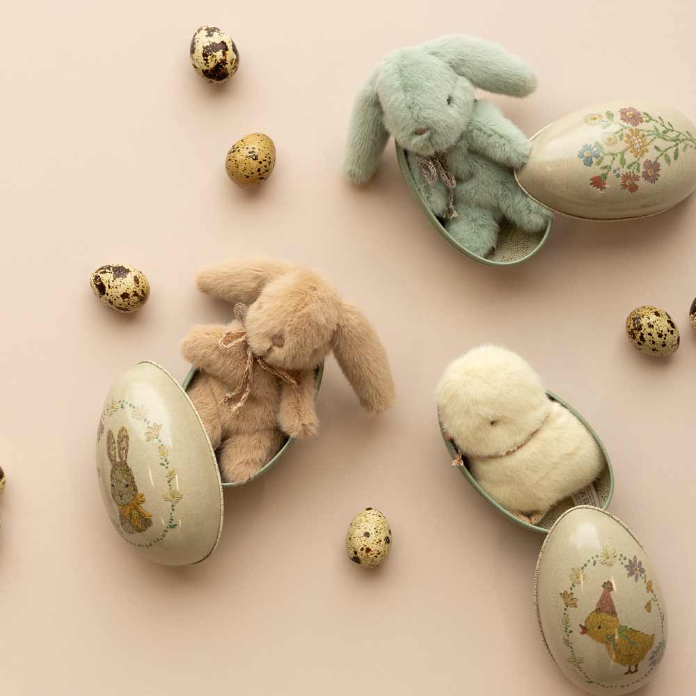 Stillleben zum Thema Ostern mit Maileg - Küken Plüsch Mini-Spielzeugen und dekorierten Eiern auf pastellfarbenem Hintergrund.