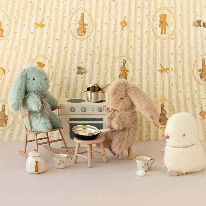 Kuscheltiere in einer verspielten häuslichen Szene angeordnet, mit zwei Maileg-Hasen, die so tun, als würden sie kochen, während ein Küken zuschaut.