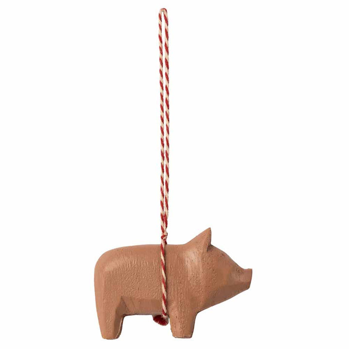 Ein Maileg-Ornament „Holzschwein-Anhänger“, das an einer rot-weißen gedrehten Schnur hängt und vor einem schlichten weißen Hintergrund abgebildet ist.