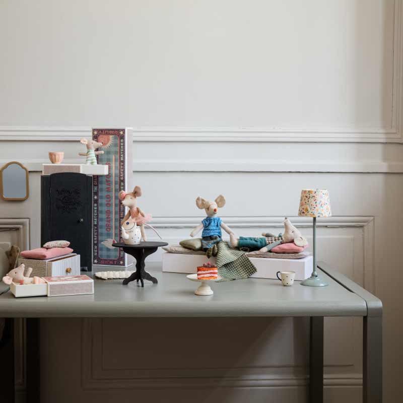 Ein geschmackvoll arrangiertes Stillleben mit der Plüschmaus „Maus Ballerina“ von Maileg, die auf einem Tisch gemütlichen häuslichen Aktivitäten nachgeht, begleitet von Büchern, Teetassen und zarten Dekorationsgegenständen.