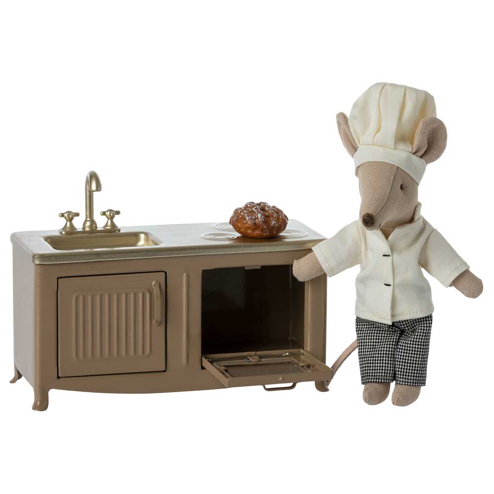 Als Koch verkleidete Maileg-Maus steht neben einer Maileg-Miniaturkücheneinheit mit Spüle und Ofen und präsentiert ein kleines Backwerk.