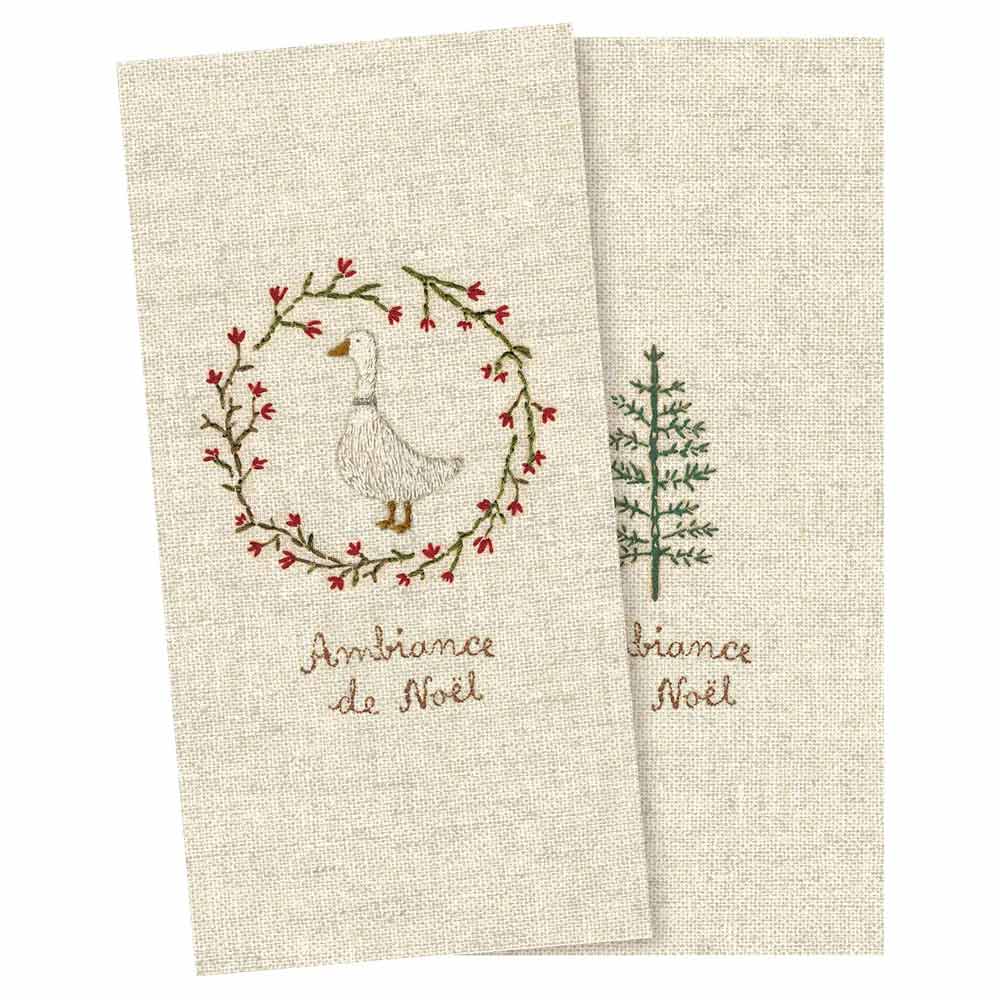 Das Produkt „Maileg - Papierservietten Gans“ umfasst zwei beige Stoffservietten mit jeweils gestickten Motiven: einmal mit einer Gans im Kranz und einmal mit einem Baum, beide geschmückt mit dem Text „Ambiance de Noël“.