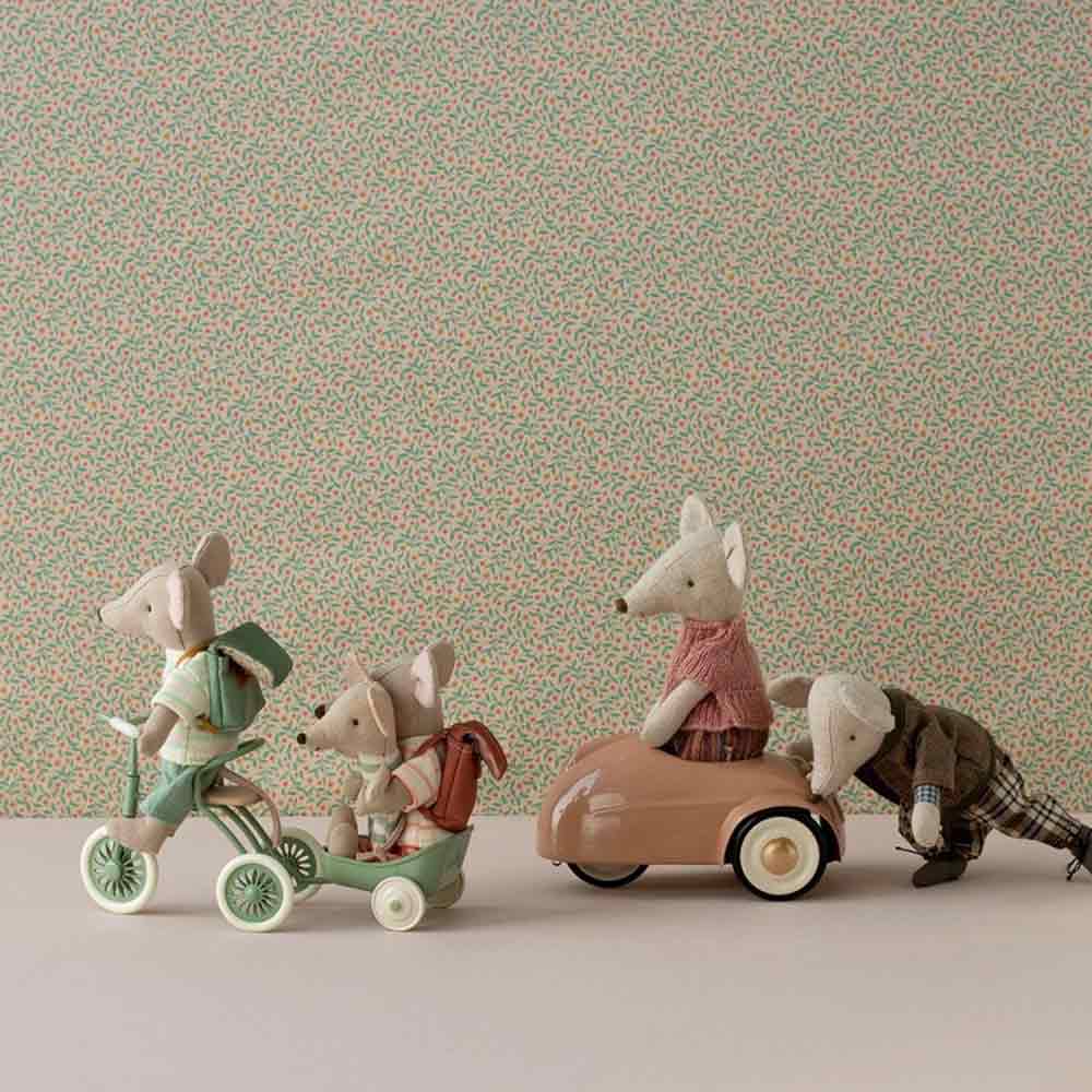 Angezogene Spielzeugmäuse fahren auf einem Maileg-Puppenhaus-Dreirad mit Garage für Maus Abri à-Dreirad und einem Auto, aufgereiht vor einem Tapetenhintergrund mit Blumenmotiv.