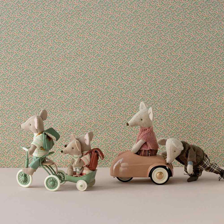 Angezogene Spielzeugmäuse fahren auf einem Maileg-Puppenhaus-Dreirad mit Garage für Maus Abri à-Dreirad und einem Auto, aufgereiht vor einem Tapetenhintergrund mit Blumenmotiv.