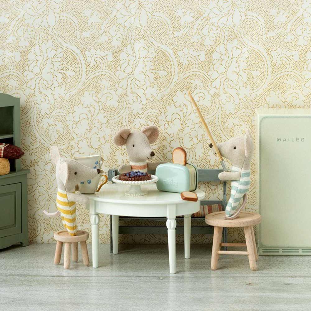 Zwei Maileg - Puppenhaus Toaster mit Toast-Mint-Puppen sitzen an einem kleinen Tisch, eine gießt Tee ein, in einem Raum mit geblümter Tapete und einem Vintage-Kühlschrank.