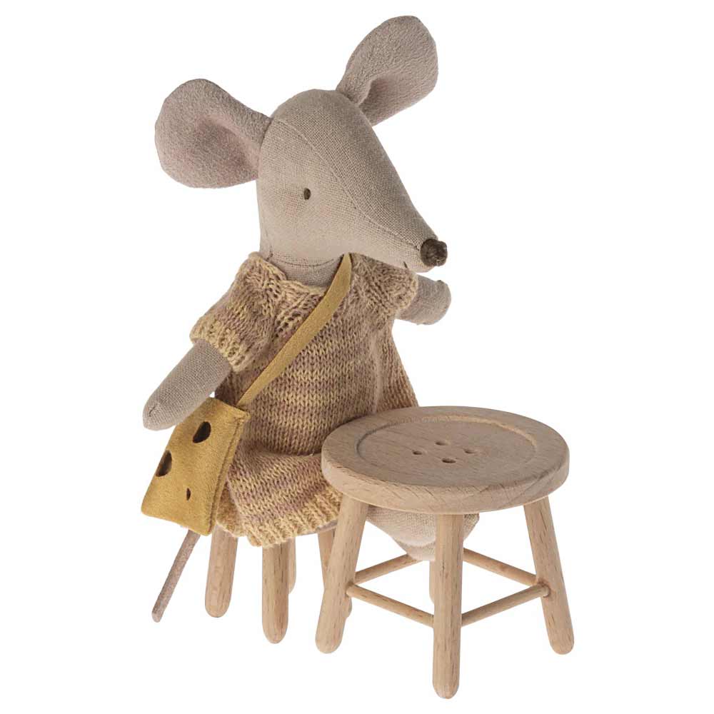 Ein Maileg - Tisch und Hocker Set Maus mit einem Strickkleid und einer gelben Tasche steht neben einem kleinen Holzhocker.