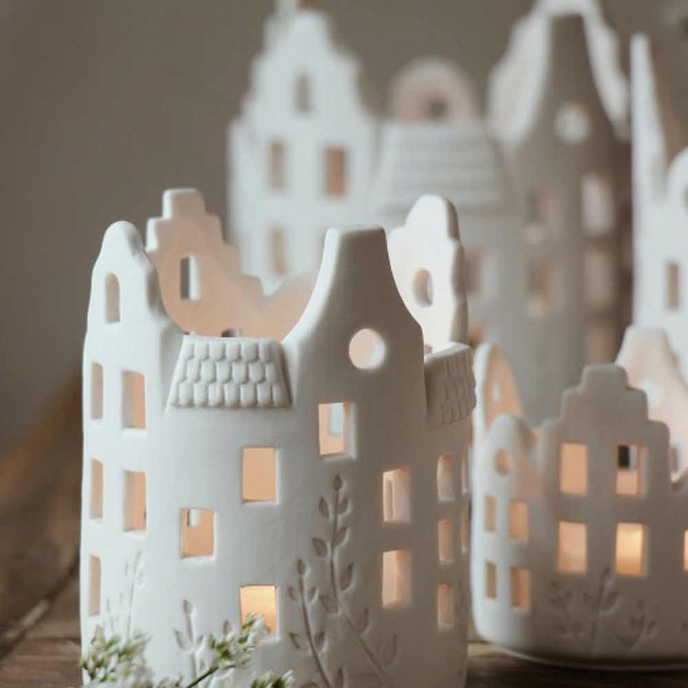 Kleine, weiße Jardin-Häuser aus Keramik von Majas Cottage - Lichthaus Keramik mit brennenden Kerzen darin, die durch ihre Fenster einen warmen Schein verbreiten.