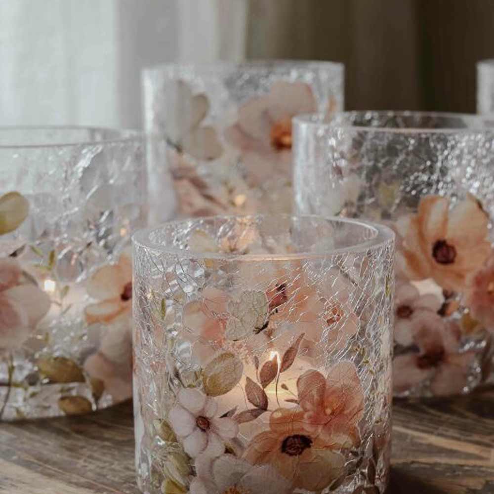 Fünf Windlicht-Kerzenhalter „Blossom & Butterflies“ von Majas Cottage mit rissiger Textur und floralem Design, jeweils mit einer brennenden Kerze darin, werden auf einer Holzoberfläche präsentiert.