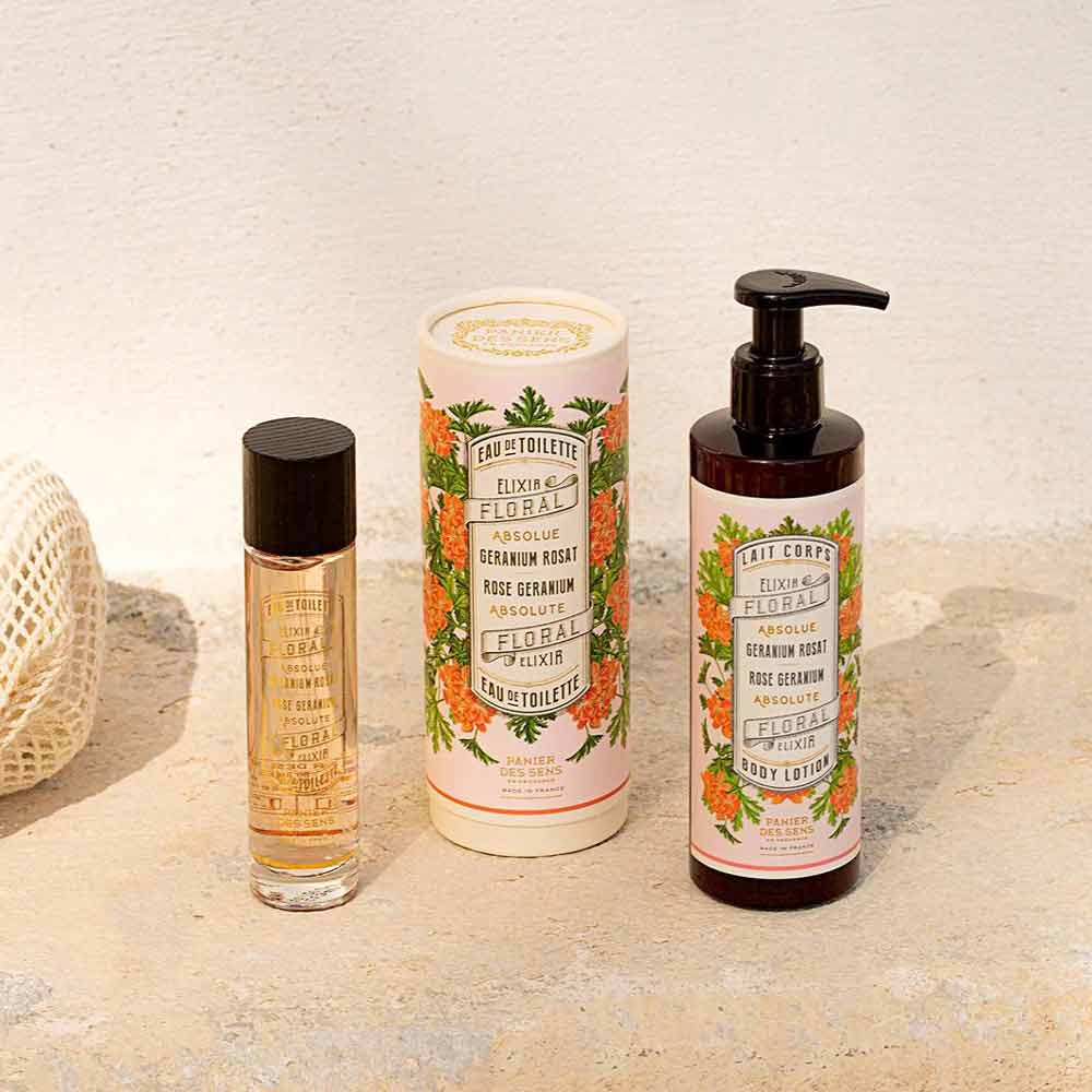 Ausgestellt werden drei Hautpflegeprodukte: ein kleines Parfümfläschchen, eine zylindrische Schachtel mit Eau de Toilette und eine Pumpflasche mit Panier des Sens – Bodylotion Rosengeranie 250 ml. Alle haben Etiketten mit Blumenmotiven und stehen auf einer hellen Oberfläche.