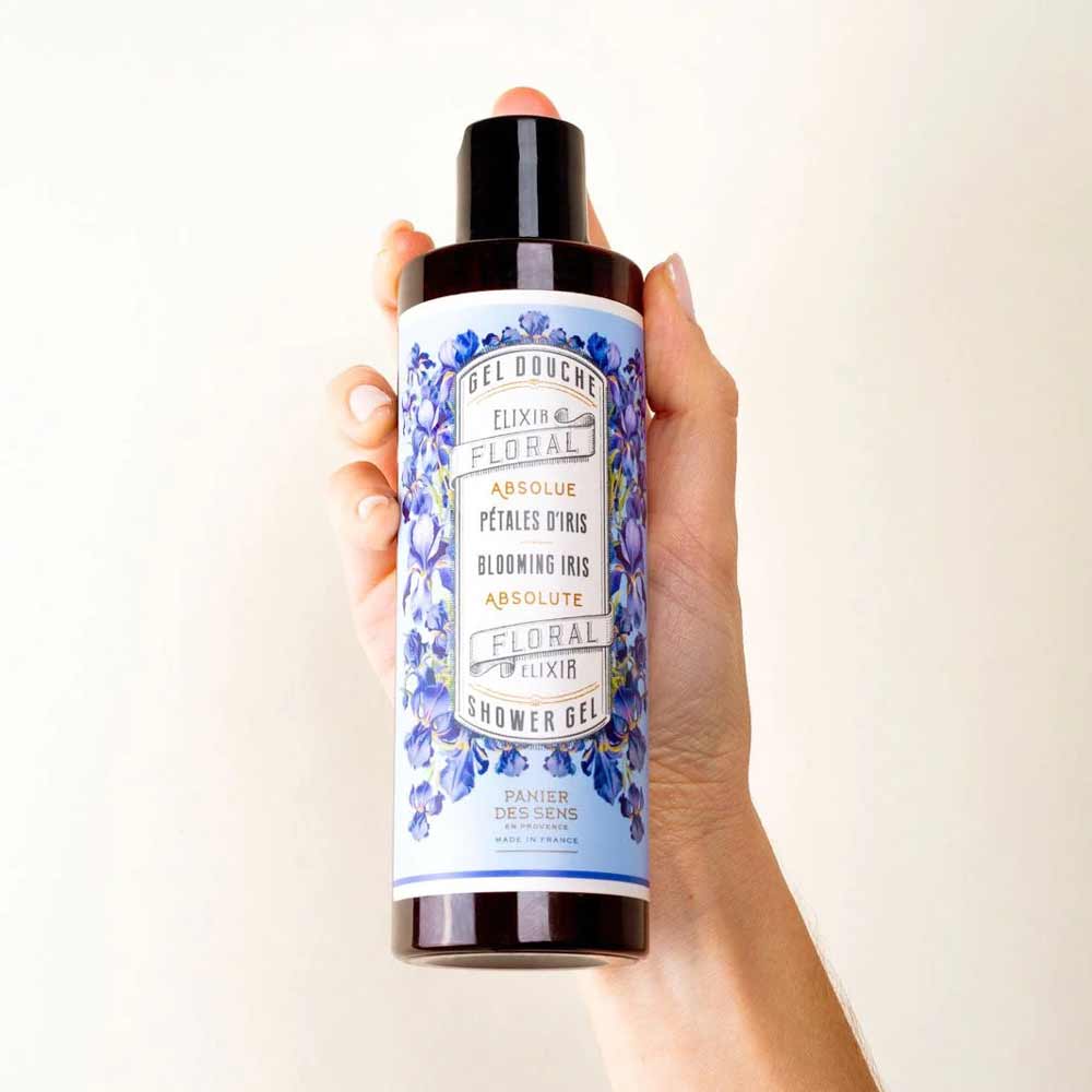 Eine Hand hält eine Flasche Duschgel mit der Aufschrift „Panier des Sens – Duschgel Irisblütenblätter 250 ml“ und einem Blumenmuster um das Etikett.