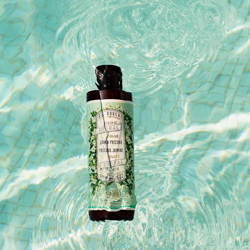 Eine Flasche Panier des Sens – Duschgel Jasmin 250 ml schwimmt in einem Becken mit klarem Wasser, wobei sich das Licht auf der Wasseroberfläche spiegelt.