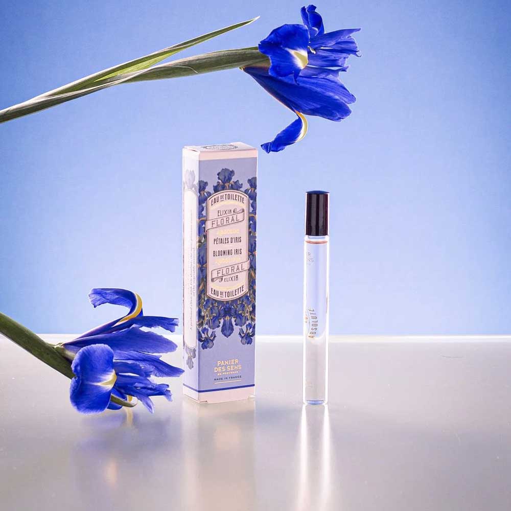Neben der Schachtel wird eine 10-ml-Flasche „Panier des Sens – Eau de Toilette Roll-on Irisblütenblätter“ präsentiert, mit zwei blauen Irisblüten im Hintergrund auf hellblauem Untergrund.