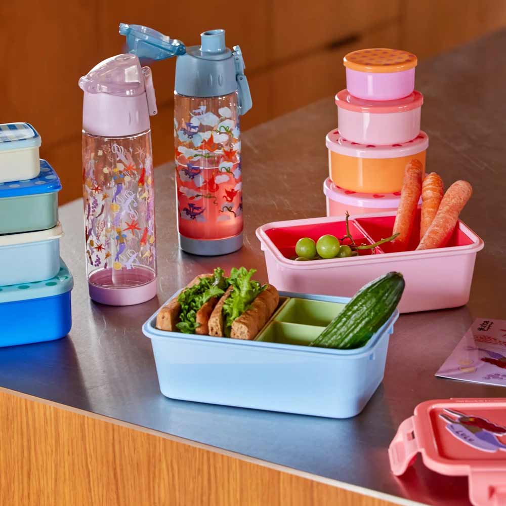 Mehrere bunte Lunchboxen, Flaschen und Reis – Lebensmittelboxen Herzen rund 4er-Set mit frischem Gemüse sind auf einer Küchentheke angeordnet.