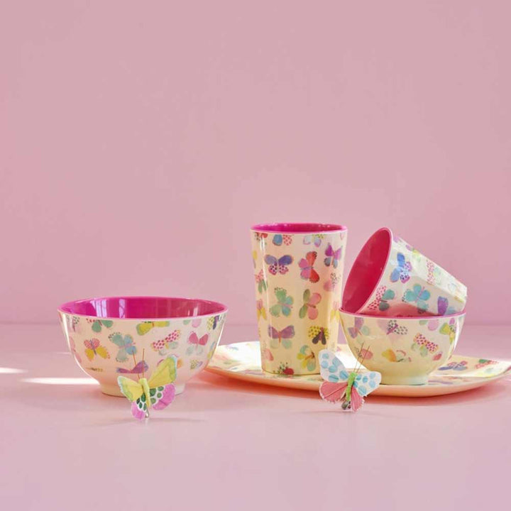 Ein Set aus rosa und gelben Rice - Melamine Latte Cup Butterfly-Tellern und -Tassen mit Schmetterlingen darauf.