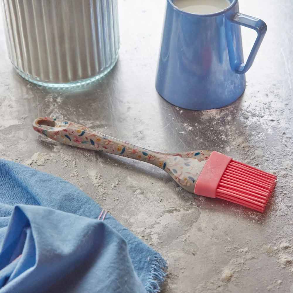 Ein Rice-Silikonpinsel „Sandy Flowers“ liegt neben einem blauen Becher und einem blauen Tuch auf einer mit Mehl bestäubten Theke.