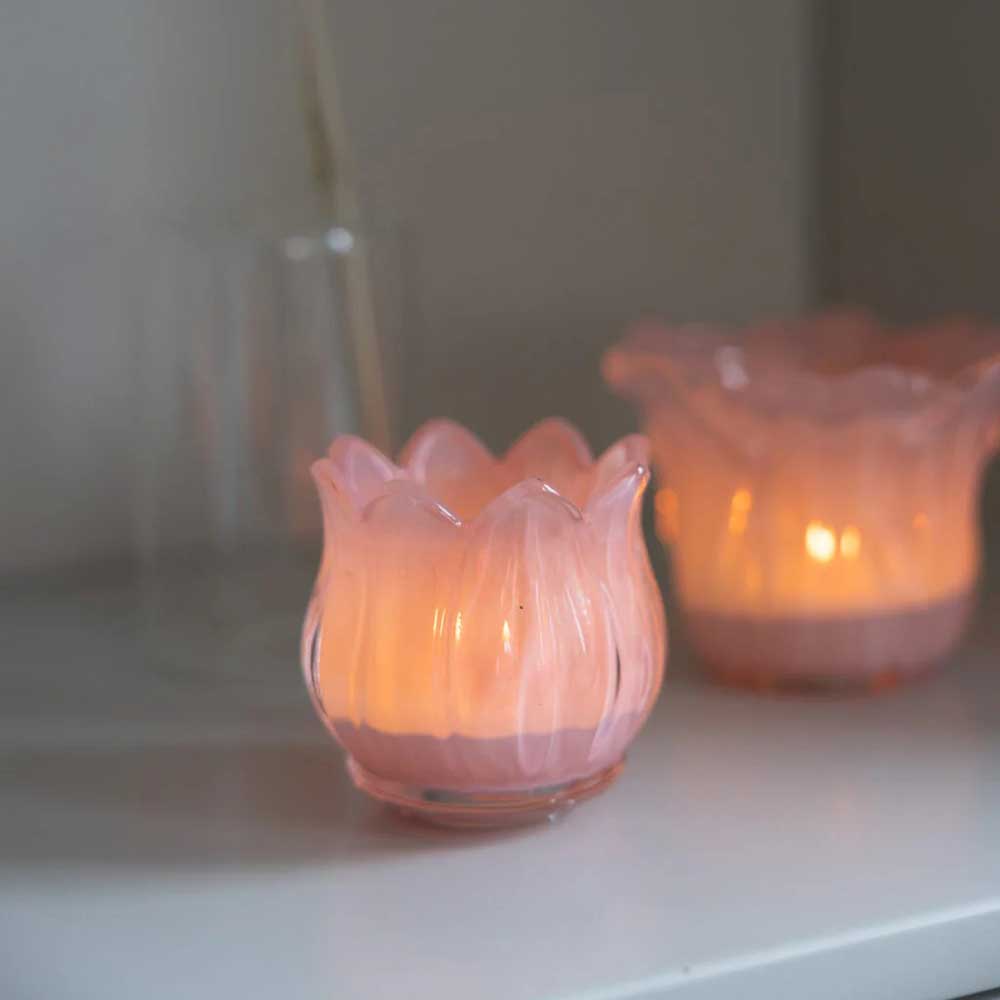 Die blumenförmigen Kerzenhalter der Storefactory – Nyby Teelichthalter Rosa in Rosa haben im Inneren brennende Kerzen, die einen sanften Schein auf die Oberfläche werfen.