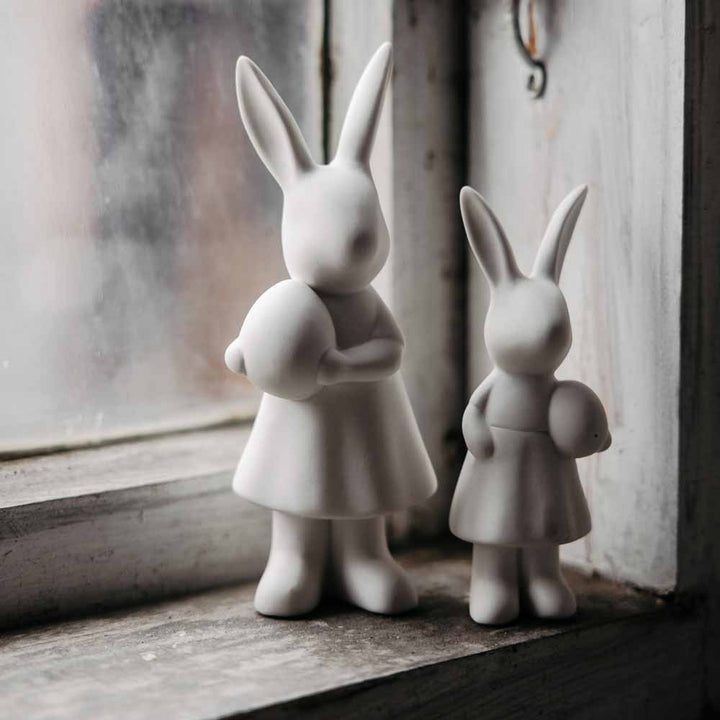Zwei weiße Storefactory-Figuren von Alice Hase vor einem nebligen Fenster.