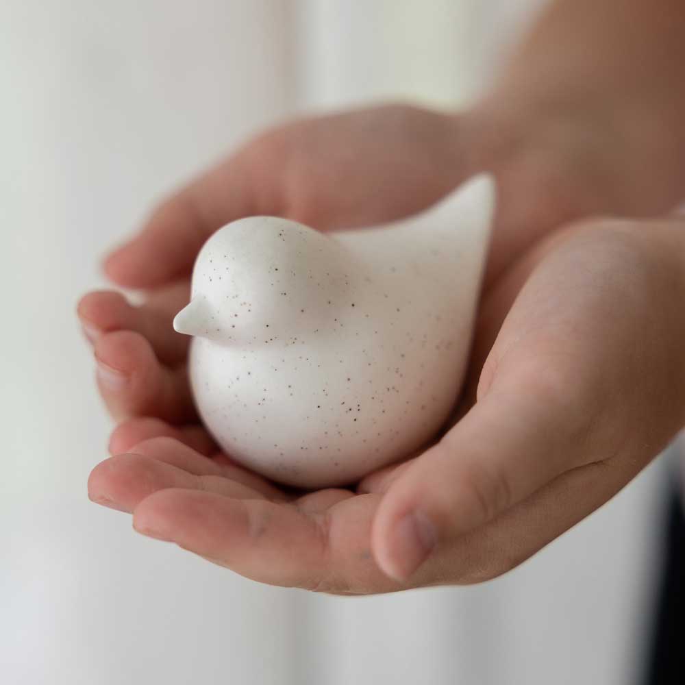 Hände halten einen Storefactory – Ellen Huhn, einen kleinen, weiß gesprenkelten Keramikvogel.