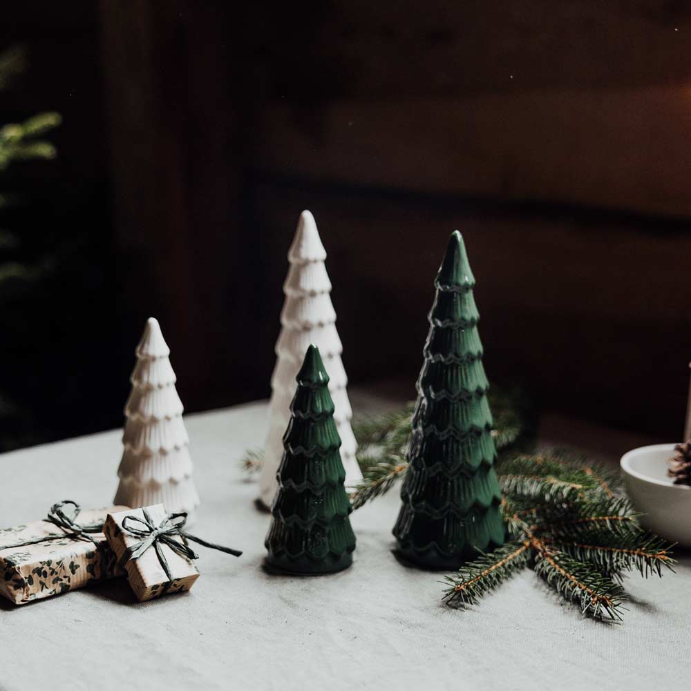 Vier Storefactory Granbacken Tannenbaum Keramikbäume, zwei weiße und zwei grüne, auf einem Tisch mit verpackten Geschenken und Tannenzweigen platziert.