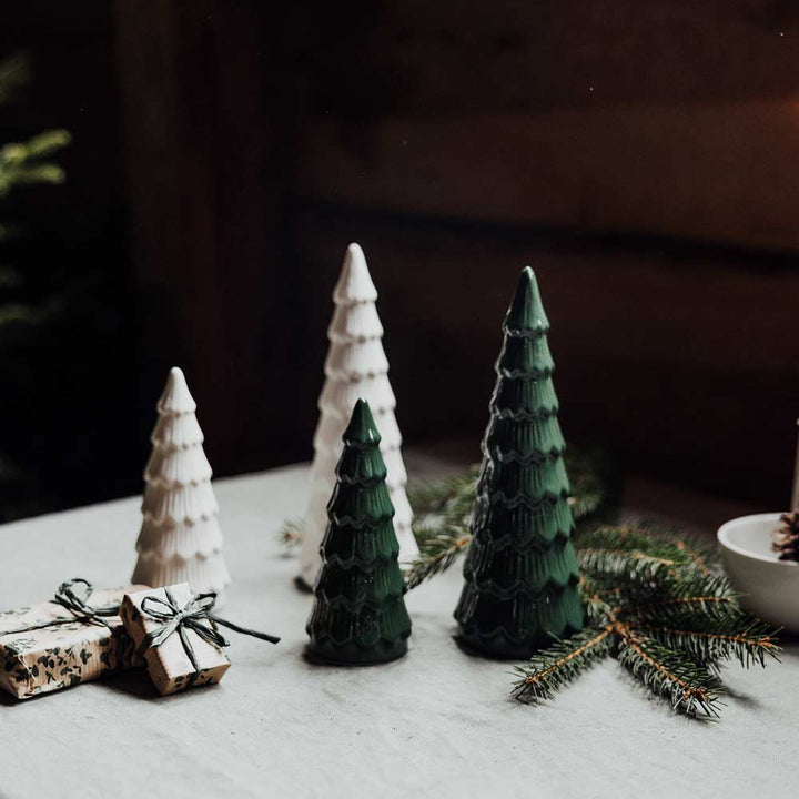 Vier Storefactory Granbacken Tannenbaum Keramikbäume, zwei weiße und zwei grüne, auf einem Tisch mit verpackten Geschenken und Tannenzweigen platziert.