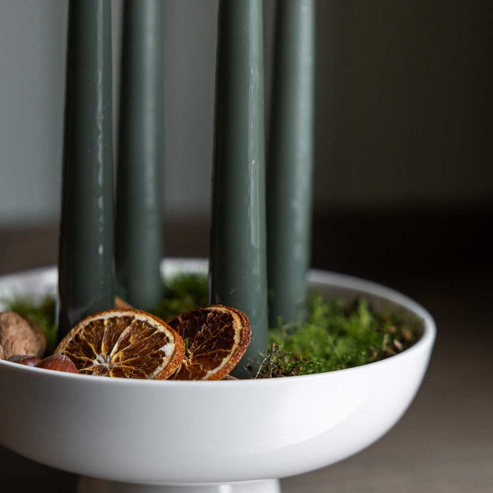 Die Storefactory - Granhammar Kerzenhalter Schale für vier Stabkerzen hält grüne Kerzen umgeben von getrockneten Orangenscheiben und grünem Moos.