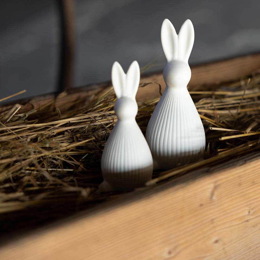 Das Storefactory – Selma Hase-Set besteht aus zwei weißen Hasenfiguren aus Keramik, die in Stroh in einem Holzbehälter eingebettet sind.