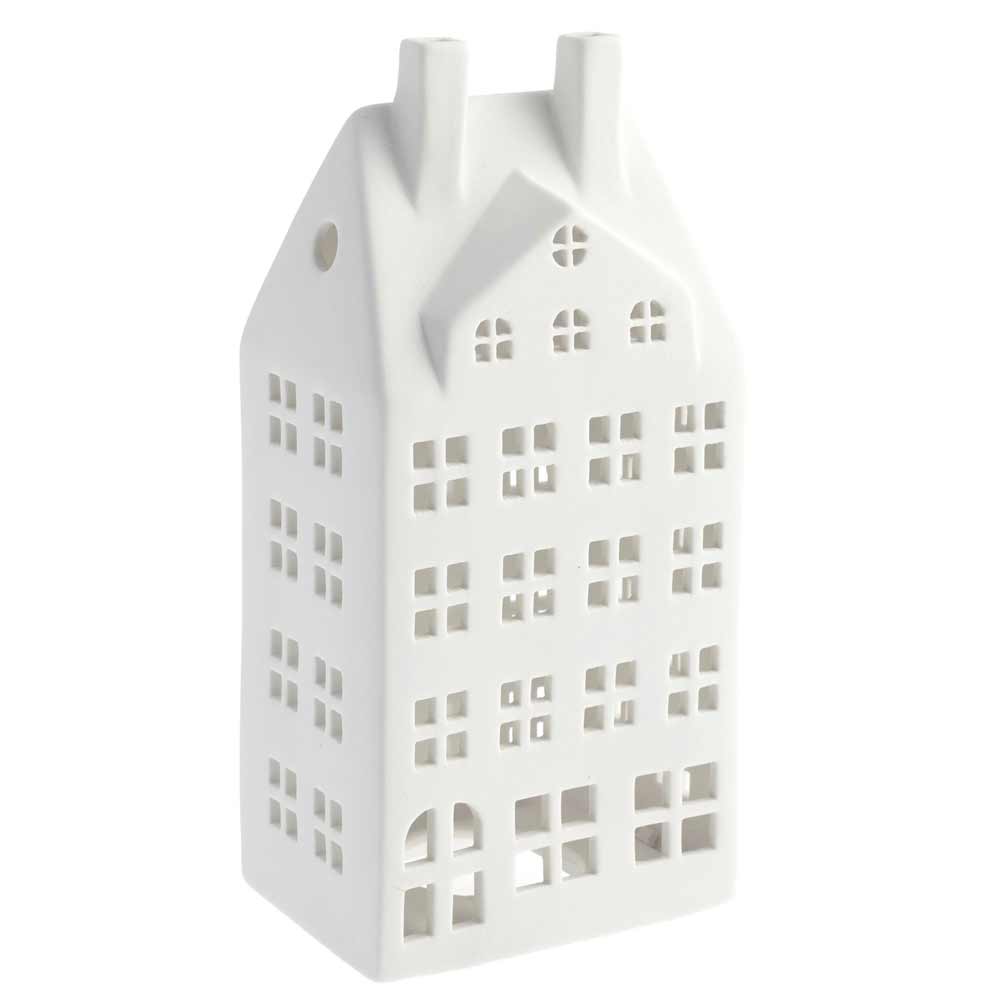 Eine weiße Keramiklaterne von Storefactory mit dem Namen Storstaden Nr. 2 Lichthaus Deko in Hausform mit mehreren Fensterausschnitten und zwei Schornsteindetails.