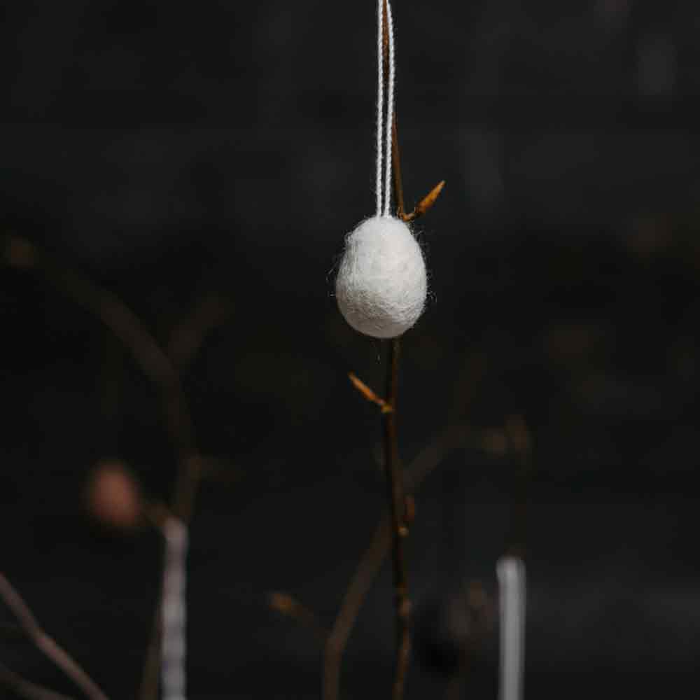 Eine Storefactory – Ullas Ei Anhänger hängt an einem Zweig auf dunklem Hintergrund.