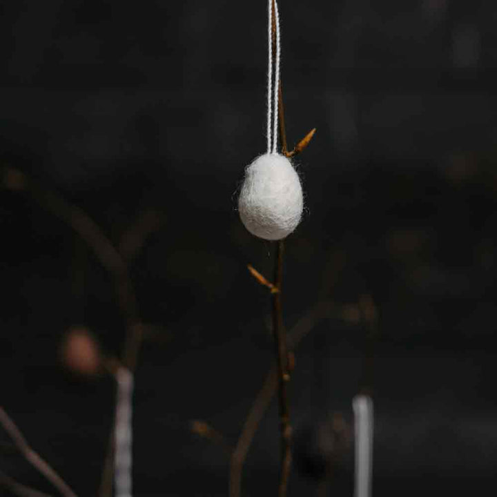 Eine Storefactory – Ullas Ei Anhänger hängt an einem Zweig auf dunklem Hintergrund.